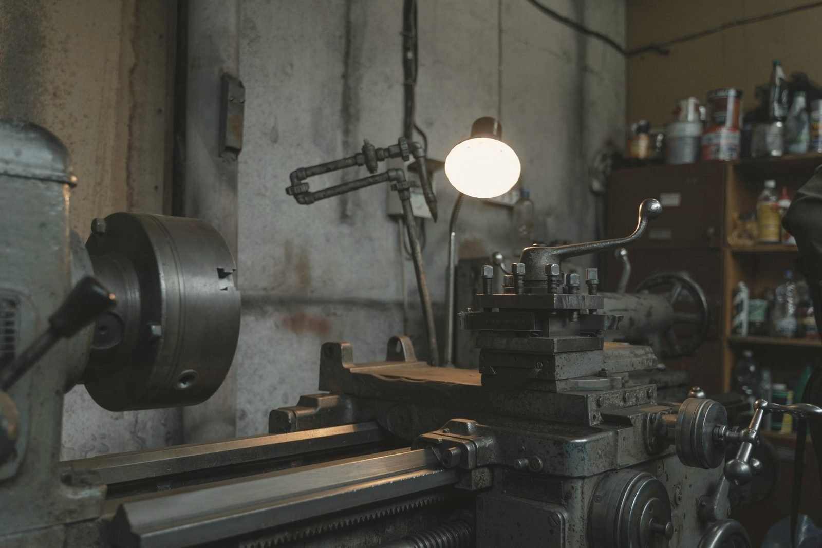 Older lathe and toolroom shelves lit by a single lamp