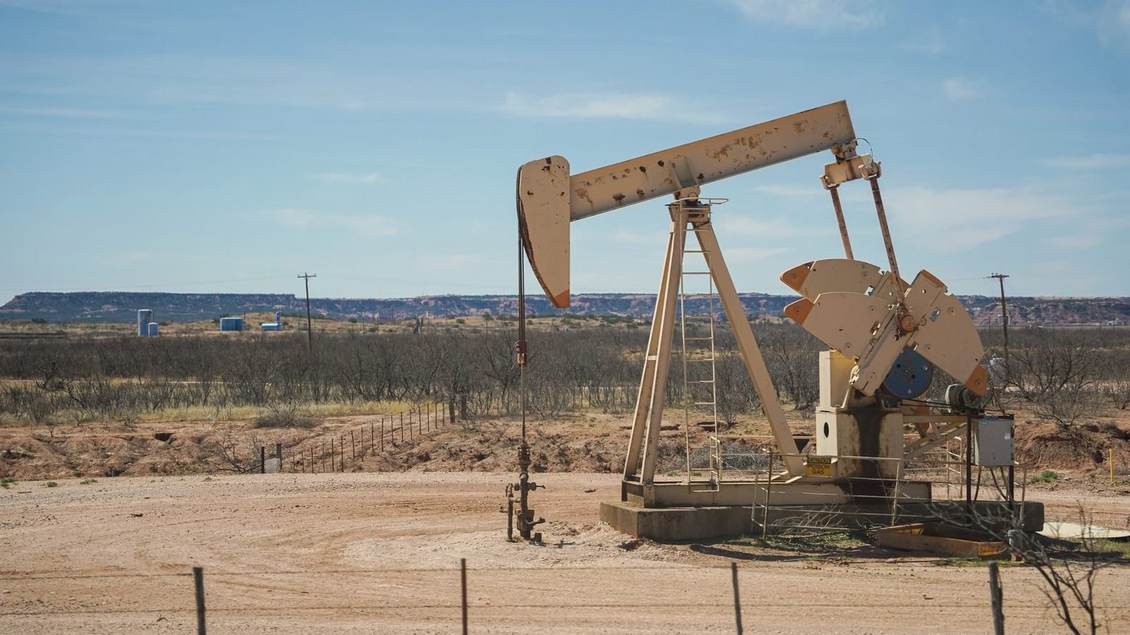 Pumping unit on a pale caliche pad under a clear midday sky